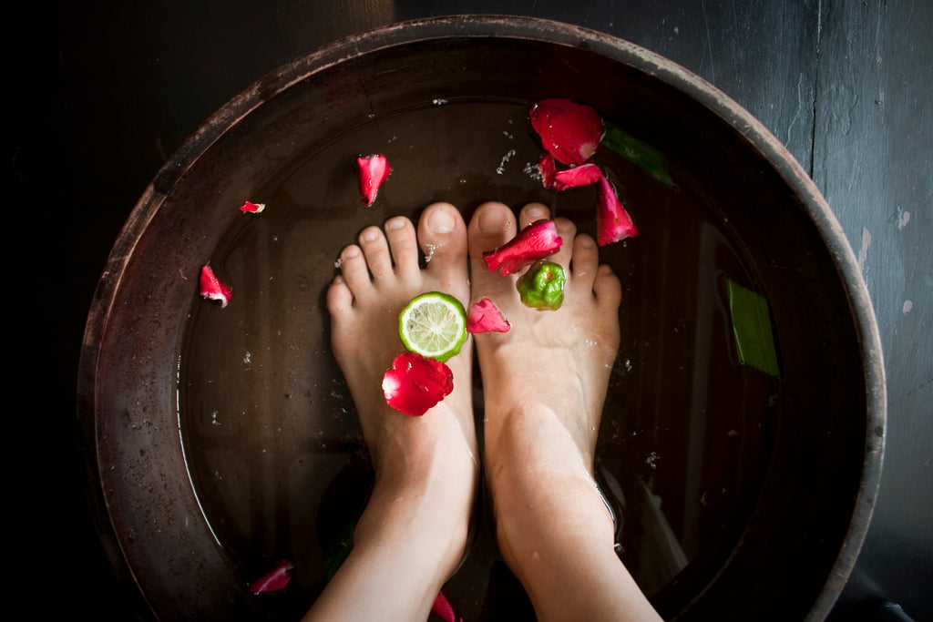 Bare feet in foot bath with flower petals and lime